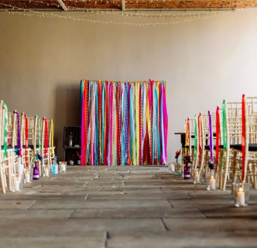 A bright and colourful ribbon backdrop shown at the end of an aisle. The chairs on each side of the aisle are decorated with ribbons to complement the backdrop.