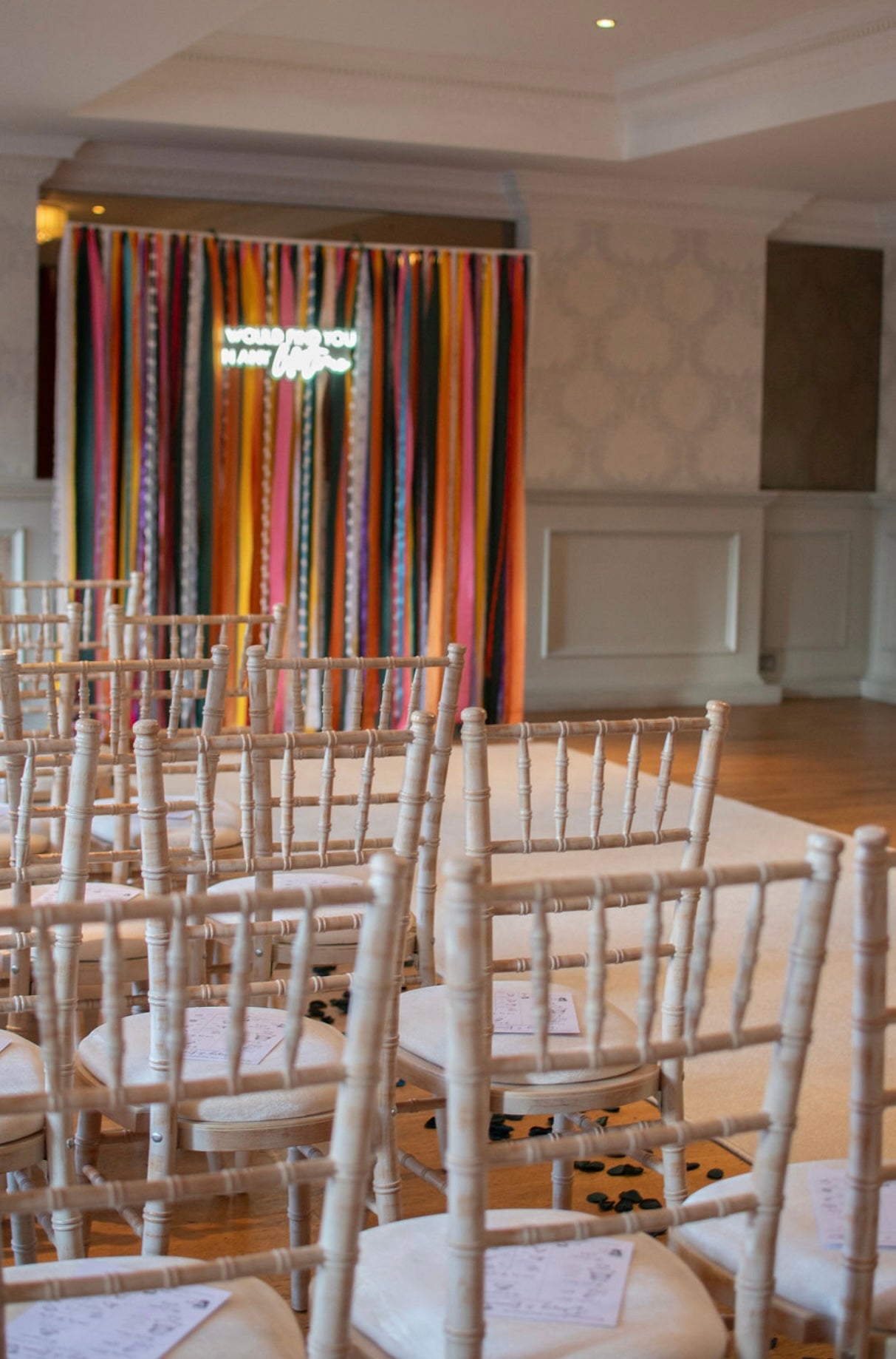 A colourful ribbon backdrop at the end of an aisle with a neon sign attached.