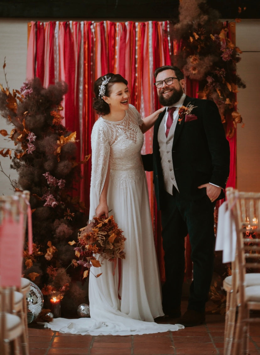 Couple standing in a decorated wedding setting with red curtains and floral arrangements.
