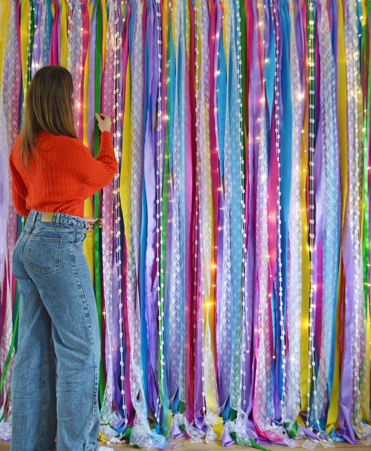 A colourful backdrop of ribbons in vibrant colours of purple, pink, yellow and blue with fairy lights. 