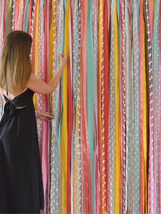 A colourful backdrop of ribbons in vibrant colours of coral, yellow and turquoise with delicate pom poms amongst the ribbons for added interest. 