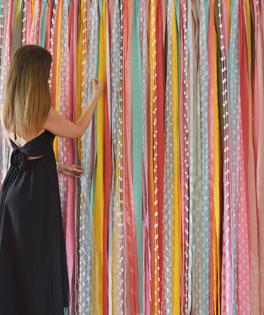 A colourful backdrop of ribbons in vibrant colours of coral, yellow and turquoise with delicate pom poms amongst the ribbons for added interest. 