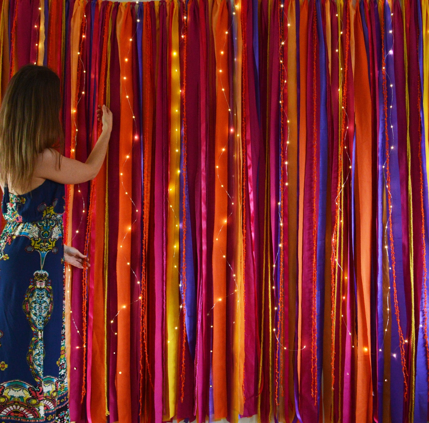 A colourful ribbon backdrop in rich, warm tones of oranges, pinks and purple with fairy lights. 