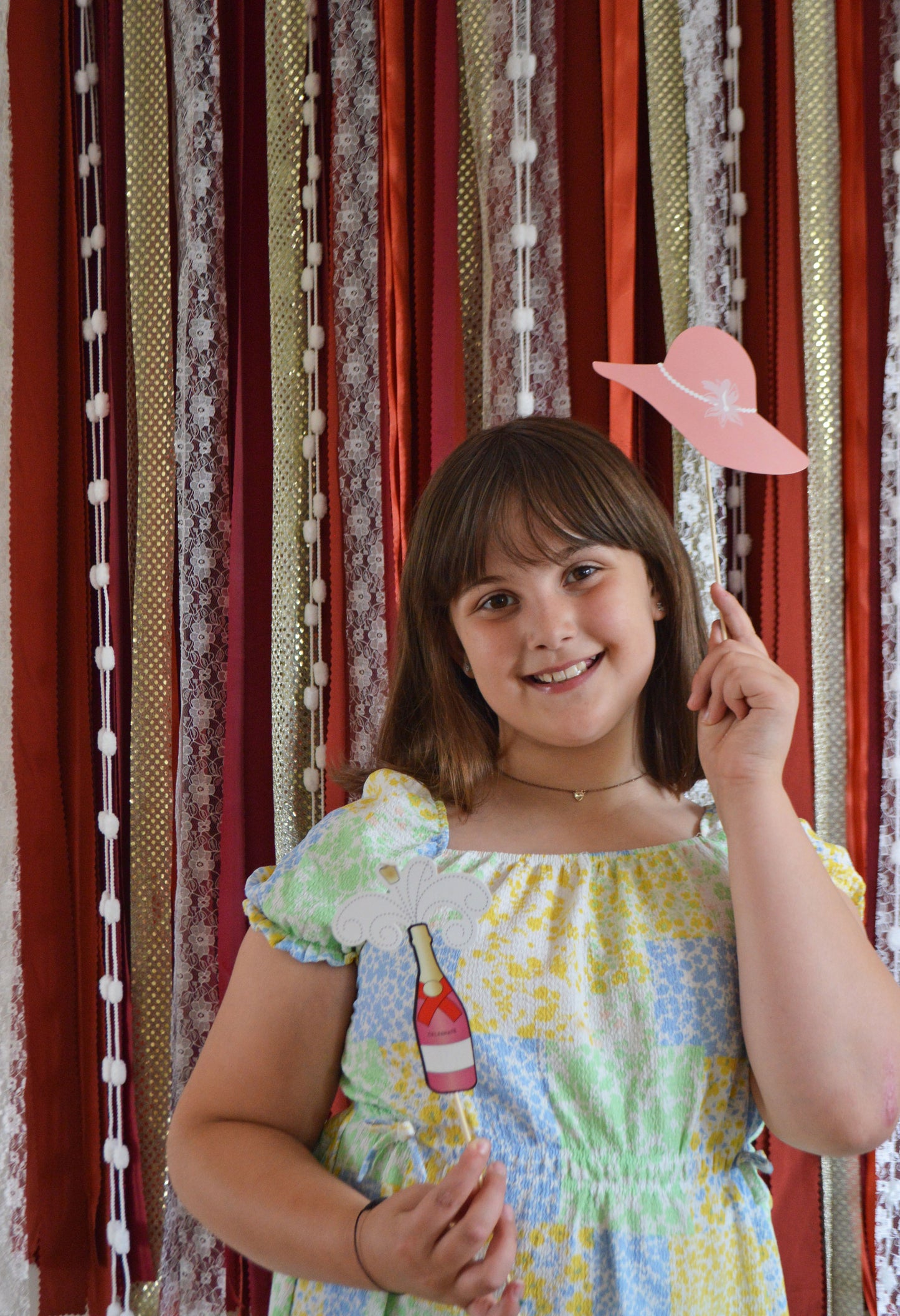 Young girl holding a pink hat in front of a striped curtain