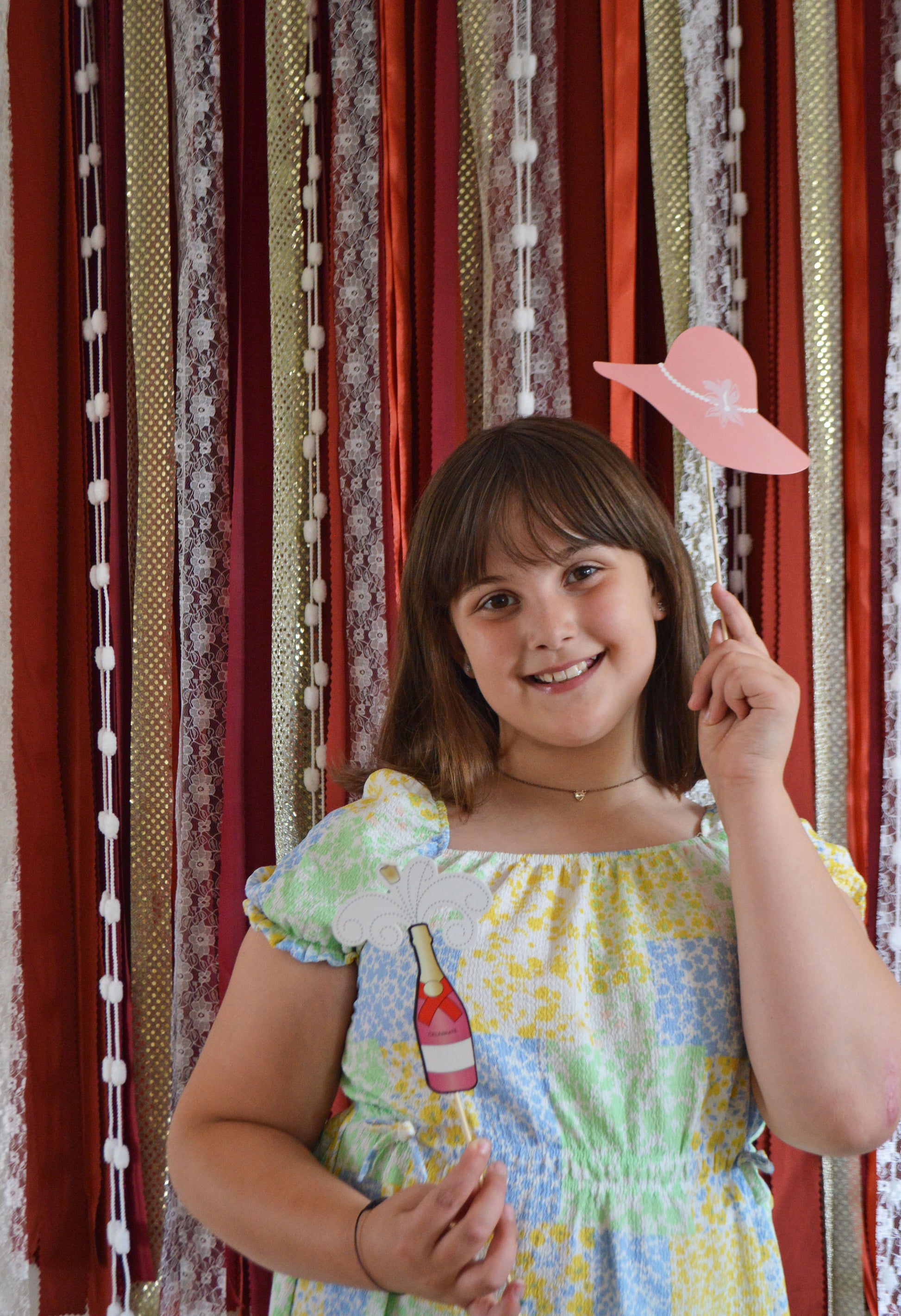 Young girl holding a pink hat in front of a striped curtain