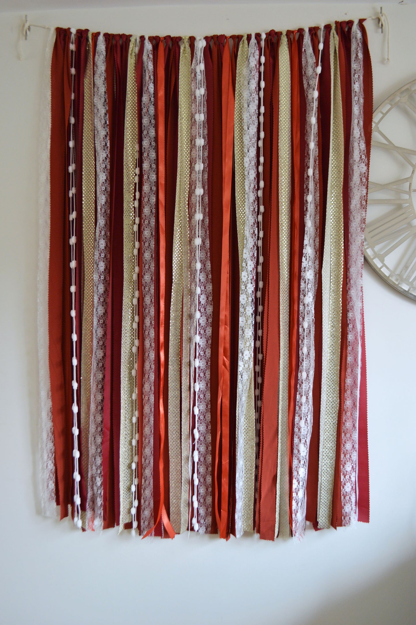 Decorative backdrop with red, beige, and white ribbons hanging against a white wall.