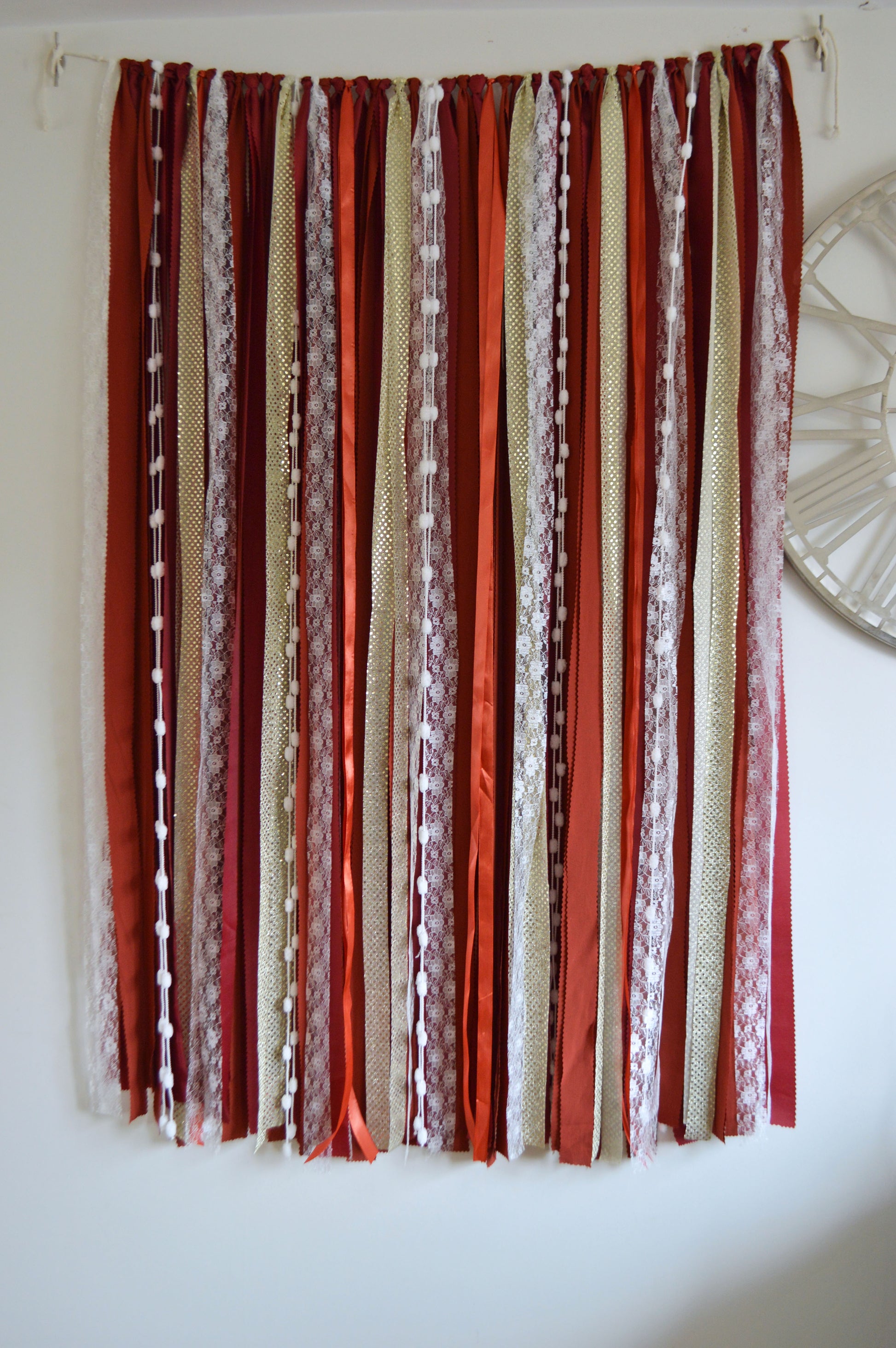 Decorative backdrop with red, beige, and white ribbons hanging against a white wall.