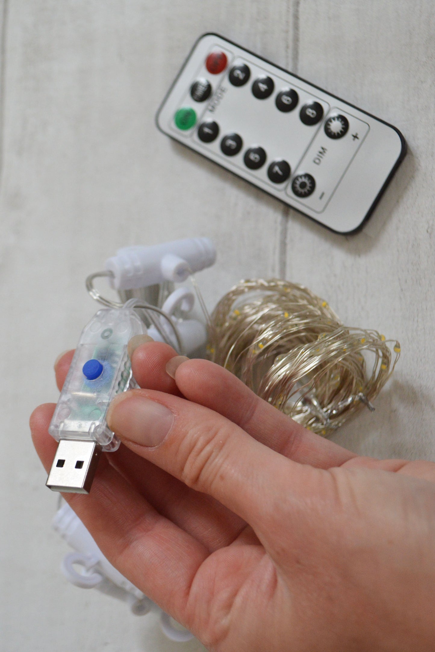 Hand holding a USB plug with a remote control for fairy lights intended to accompany our ribbon backdrop.