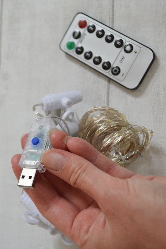 Hand holding a USB plug with a remote control for fairy lights intended to accompany our ribbon backdrop.